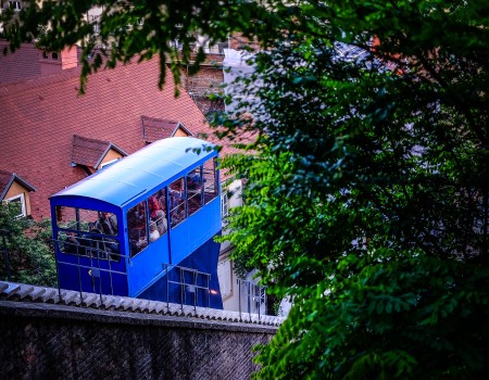 Zagreb's historic funicular ascending a steep incline, surrounded by buildings and lush greenery, connecting the Upper and Lower Towns.